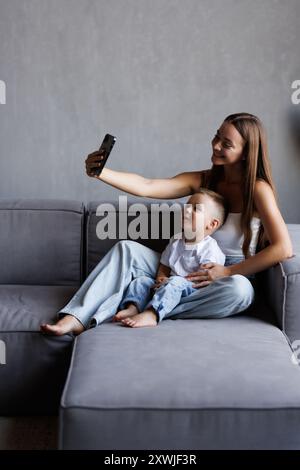 Joyful young woman holding mobile phone, taking selfie shot with small cute kid boy. Smiling female blogger recording funny video vlog with adorable c Stock Photo