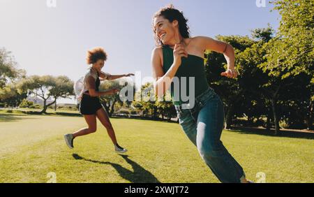 Energetic girlfriends running and playing tag in a park on a sunny summer day, enjoying a fun time together outdoors. Stock Photo