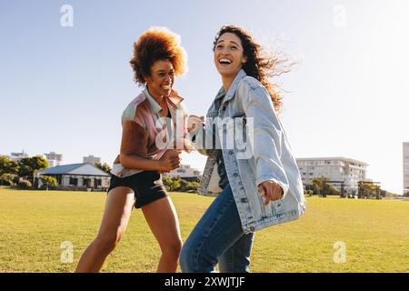 Two energetic girlfriends laughing and having fun together in the city park, showcasing happiness and friendship. Stock Photo