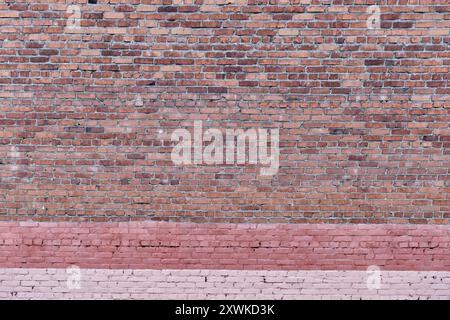 Red brick wall texture as abstract background. Old shabby dirty surface with painted pink stripes at bottom Stock Photo