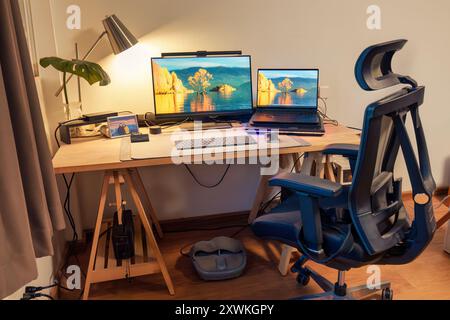 Interior workplace of photographer with laptop, monitor, computer device, lighting lamp, green leaf on wooden table and ergonomic chair in the house Stock Photo