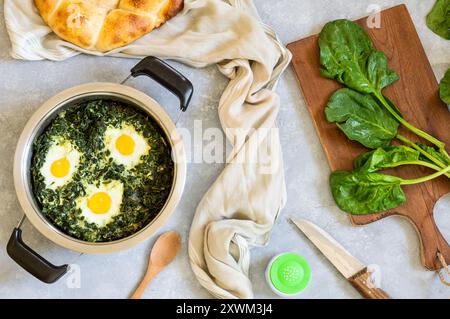 Roasted spinach and fried eggs in stewpot with fresh spinach vegetable on rustic table Stock Photo