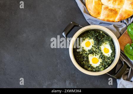 Roasted spinach and fried eggs in stewpot with fresh spinach vegetable on rustic table Stock Photo