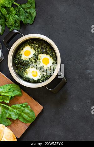 Roasted spinach and fried eggs in stewpot with fresh spinach vegetable on rustic table Stock Photo