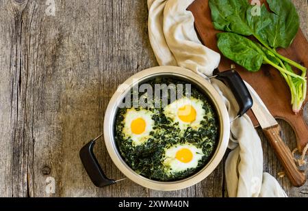 Roasted spinach and fried eggs in stewpot with fresh spinach vegetable on rustic table Stock Photo