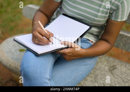 Woman finds creative flow, jotting down ideas in her notebook while enjoying the peace of a park bench. Stock Photo