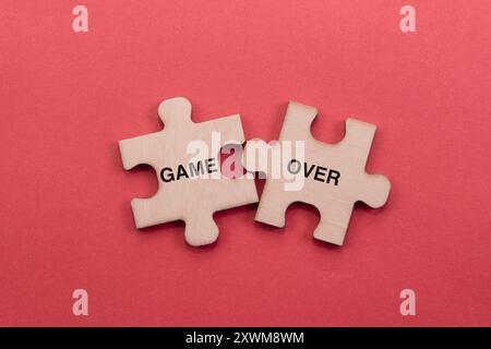 Two wooden puzzle pieces spell out the words "GAME OVER" on a vibrant red background. Stock Photo