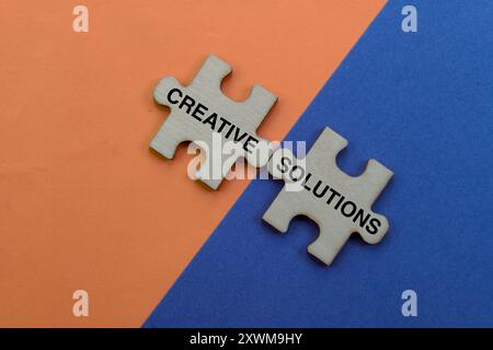 Wooden puzzle pieces connect to reveal "Creative Solutions" on vibrant orange and blue background. Stock Photo