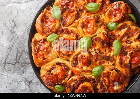 Swirl pie with tomato sauce, cheese, Italian sausages and basil close-up in baking dish on table. Horizontal top view from above Stock Photo