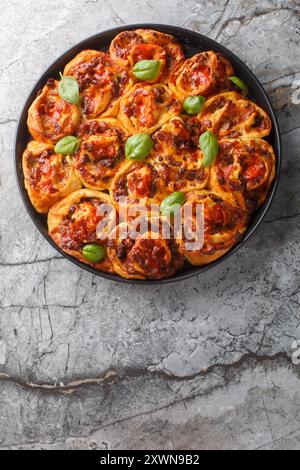 Hot pizza roll with tomatoes, cheese, Italian sausages and basil close-up in baking dish on table. Vertical top view from above Stock Photo