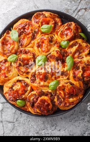 Italian pizza roll with tomatoes, cheese, sausages and basil close-up in baking dish on table. Vertical top view from above Stock Photo