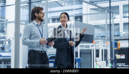 Portrait of an Experienced Male and Female Engineers Walking in Agency Room, Using Computer Tablet Device and Discussing Production at a Modern Automated Electronics Manufacture with Robotic Arms Stock Photo