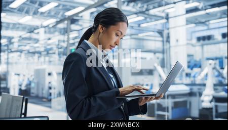 Portrait Of Electronics Manufacturing Technician Working on a Laptop Computer at a Factory Space. Asian Female Specialist Developing, Maintaining, and Fine-Tuning Programs for Production and Assembly. Stock Photo