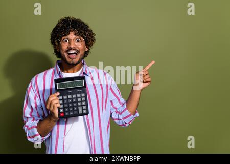 Photo of ecstatic smart guy dressed shirt in glasses hold calculator indicating at sale empty space isolated on khaki color background Stock Photo