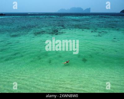 Traveler swimming in the middle of the tropical waters of Phi Phi Don with Phi Phi Le in the background Stock Photo