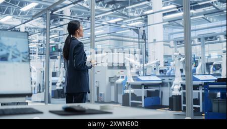 Electronics Manufacturing Technician Working on Tablet Computer at a Factory Space. Asian Female Specialist Developing, Maintaining, and Fine-Tuning Programs for Machine Production and Assembly Stock Photo