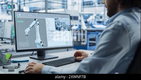 System Administrator Working on a Desktop Computer at Modern Manufacturing Plant. Software Developer Programming the Work of the Robotic Arms, Monitoring Production on the Assembly Conveyor Stock Photo