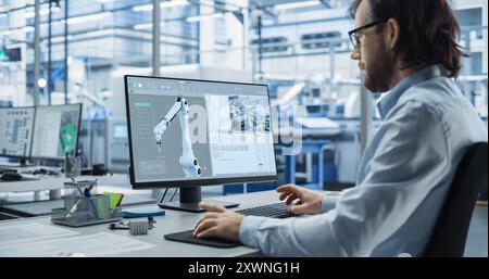 System Administrator Working on a Desktop Computer at a Modern Manufacturing Plant. Software Developer Programming the Work of the Robotic Arms, Monitoring Production on the Assembly Conveyor Stock Photo