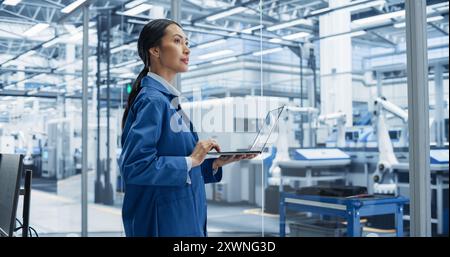 Southeast Asian Engineer Using Laptop Computer and Looking Around a Factory Facility with Equipment Producing Modern Electronic Components for Advanced Industrial Productions Stock Photo