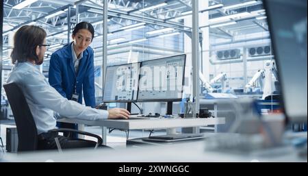 Portrait of a Young Male Engineer and a Asian Team Leader Collaborating on a Project, Using Computer and Talking in a Factory with Equipment Producing Modern Technical Devices for Tech Industries Stock Photo