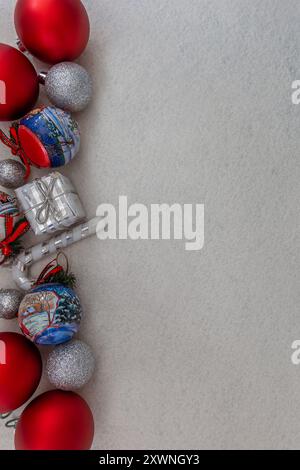 Flat lay of red and silver Christmas ornaments, candy cane, and gift box arranged vertically on a white textured background. Empty space for text Stock Photo