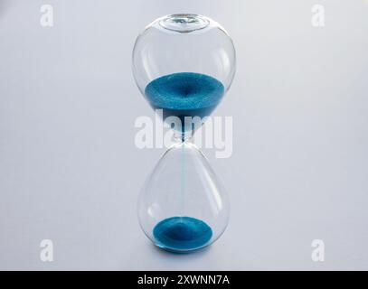 Hourglass containing blue sand isolated on white background. Concept of time passing Stock Photo
