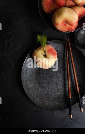 Overhead view of a bowl of flat peaches and a peach on a plate with chopsticks Stock Photo