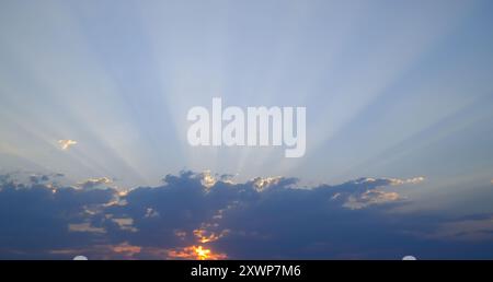 Dramatic sunset with sunbeams breaking through clouds. Scenic sky landscape, nature background, atmospheric evening light. Stock Photo
