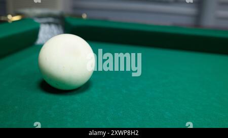 Single white billiard ball on green felt table. Close-up of cue ball, pool game equipment, sports and recreation theme. Stock Photo