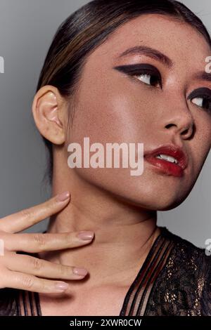 A close-up of an Asian woman with dark eyeliner, wearing a black lace top, gazing off to the side. Stock Photo