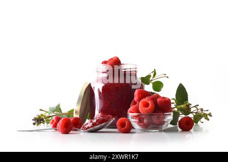 Jar of raspberry jam isolated on white background with fruit around it reflected in the base. Front view. Stock Photo