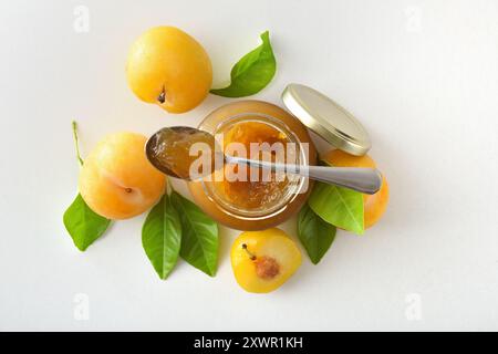 jar and spoon full of plum jam and fruit around isolated on white table. Top view. Stock Photo