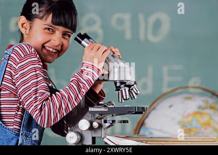 A Portrait of a smiling girl examines samples through a microscope in a Science classroom Stock Photo