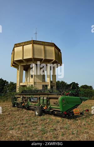 The Gosbeck concrete water tower stands in the summer sun as a table from a combined harvester is resting on its trailer between harvesting. Stock Photo