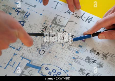 Close-up of hands using pens to point at details on an architectural blueprint. The image conveys teamwork, planning, and precision, which can be a metaphor for collaboration and detailed project management. Stock Photo
