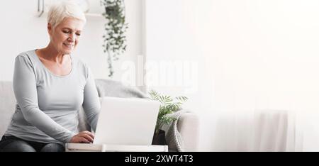 Cheerful senior lady using laptop on sofa at home Stock Photo