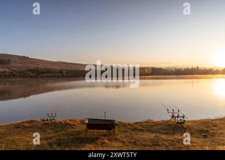 Carp fishing rods with carp bite indicators and reels set up on rod pod near lake river. Fishing during sunrise. Stock Photo