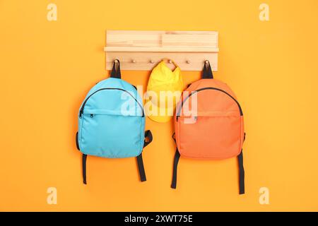 Bright backpacks and cap hanging on orange wall Stock Photo
