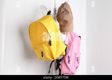 Bright backpacks and cap hanging on white wall Stock Photo