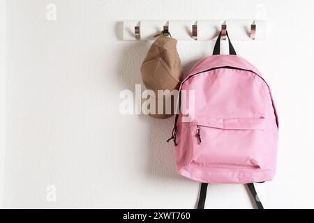 Pink backpack and cap hanging on white wall, space for text Stock Photo