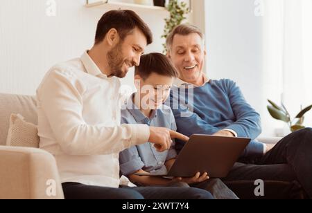 Boy Using Laptop Sitting Between Father And Grandpa At Home Stock Photo