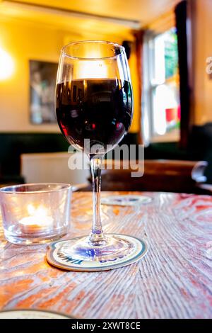 closeup of glass of red wine  on wooden table in cosy british pub Stock Photo