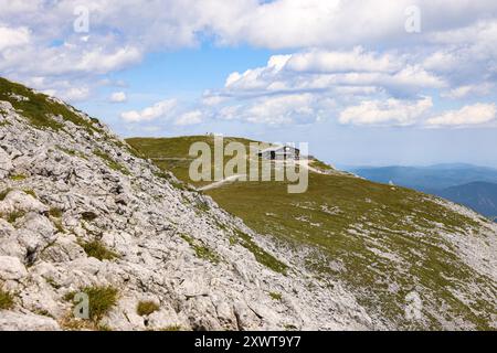 A view of the Fischerhütte, an alpine hut located near the summit of Schneeberg in Austria. The hut sits atop a gently sloping grassy ridge, surrounde Stock Photo