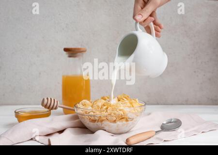 Woman adding milk in bowl with tasty cornflakes on table Stock Photo