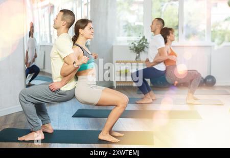Group of men and women doing acroyoga exercises in pairs, exercising partner yoga during training in fitness center Stock Photo