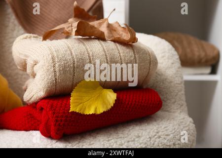 Warm sweaters with autumn leaves on armchair in room, closeup Stock Photo