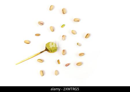 Pistachio nuts scattered around a gold spoon with green pistachio paste on a white background Stock Photo