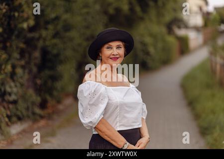 A woman poses confidently on a nature path, wearing a white blouse and black skirt, with soft sunlight highlighting her features. Stock Photo