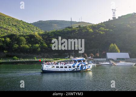 Rio Douro - Cais de Bagaúste, Portugal - October 05, 2023: Cruise boat on the Douro River going down the river with the Bagaúste pier and the mountain Stock Photo