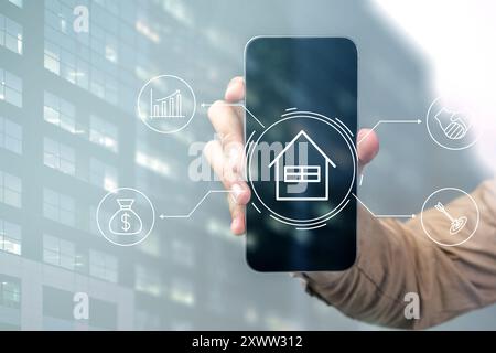 A person is holding a cell phone that has a house icon on it. The phone is displaying a house and a few other icons Stock Photo